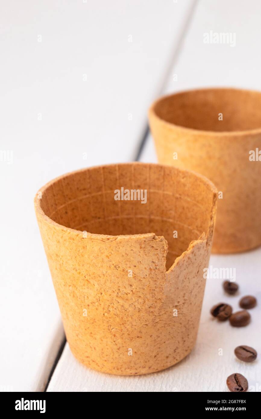 Tasses à café gaufré comestibles avec grains de café rôtis sur une table en bois blanc. Concept zéro déchet Banque D'Images