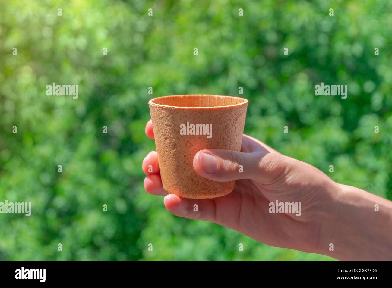 Tenir à la main une tasse à café alvéolé comestible sur fond vert. Concept zéro déchet Banque D'Images