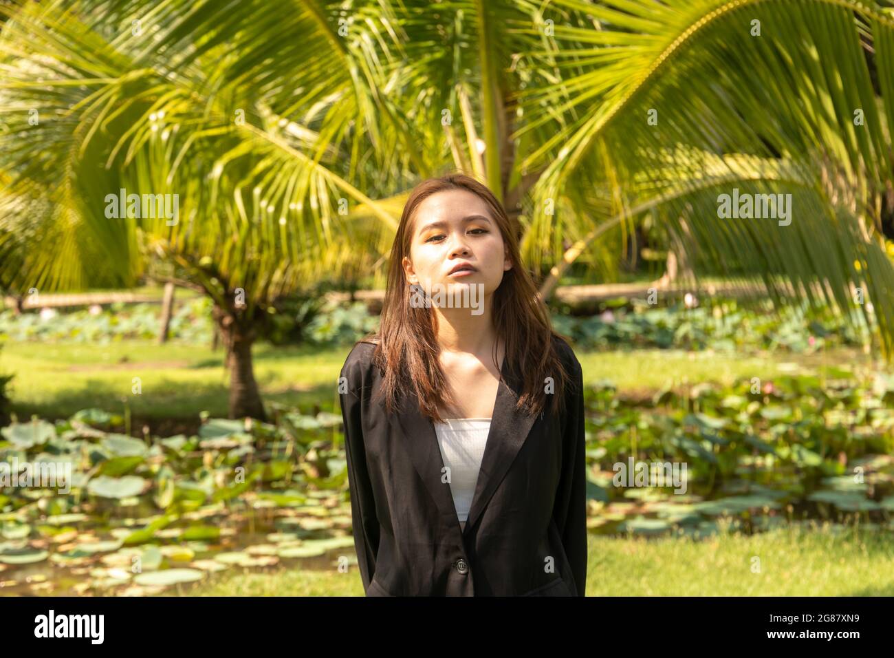 Une jeune femme d'Asie du Sud portant un manteau habillé noir pose sérieusement dans le parc Banque D'Images