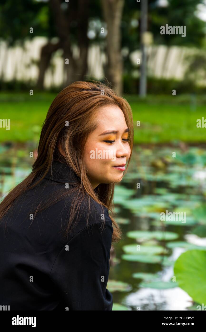 Portrait d'une jeune femme d'Asie du Sud qui se pose à côté d'un étang avec des nénuphars dans le parc Banque D'Images