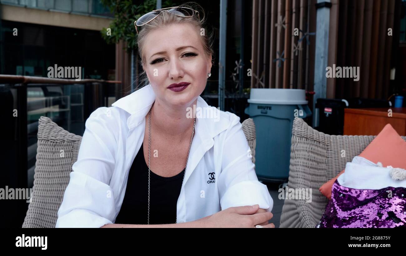 Blonde caucasienne Belle dame porter une veste blanche sur un chemisier noir assis à la table à l'extérieur Banque D'Images