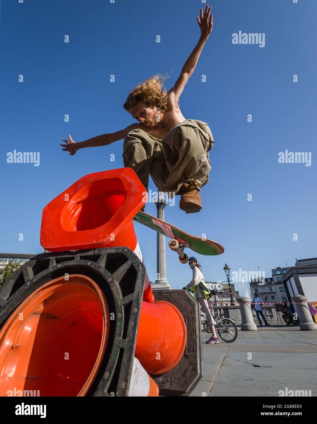 Un cycliste regarde comme un skateboarder saute sur des cônes dans Trafalgar Square. Banque D'Images
