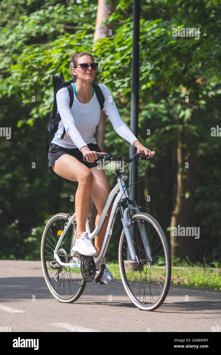 Belle blonde blanche grande fille avec short blanc, lunettes de soleil et  vélo dans le parc en été, vertical Photo Stock - Alamy