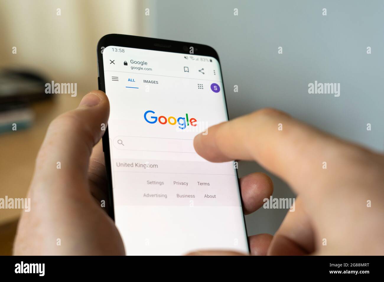 Main d'un homme tenant un smartphone Android à la maison et sélectionnant la barre de recherche Google sur la page d'accueil du moteur de recherche google.com Banque D'Images
