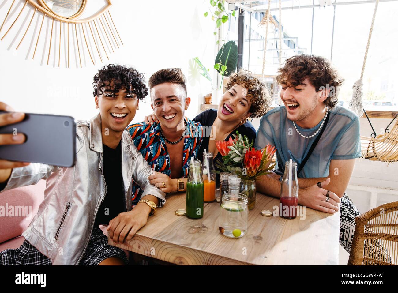 Quatre amis prenant un selfie tout en s'asseyant ensemble pendant le déjeuner. Groupe de jeunes queer souriant gaiement dans un restaurant. Amis liant et Banque D'Images