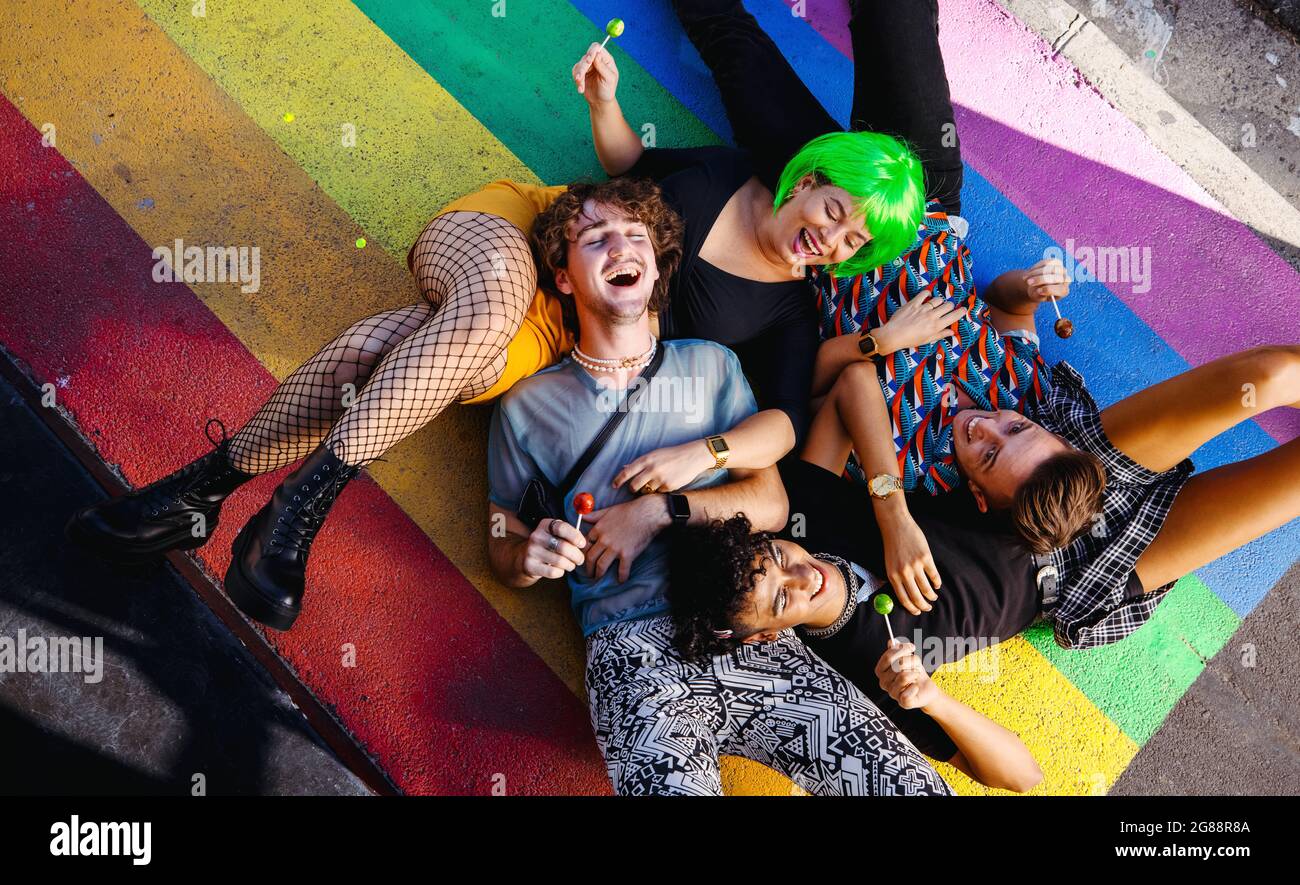 Quatre jeunes reines couchés ensemble sur des couleurs arc-en-ciel. Groupe de personnes heureux LGBTQ+ souriant gaiement pendant que chacun tient un lollipop. Amis Banque D'Images