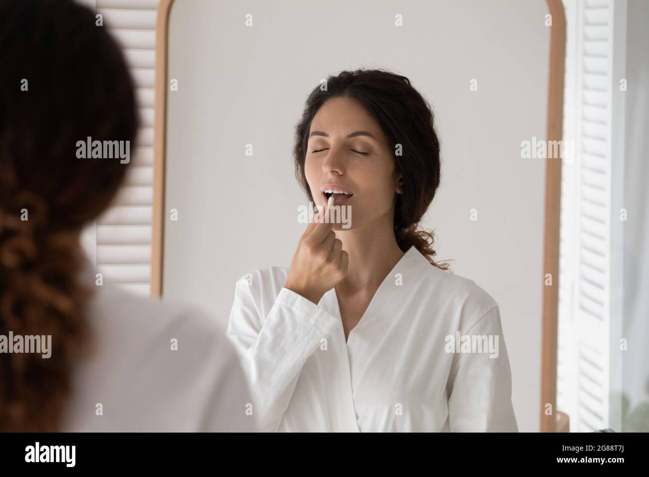 Jeune femme latine debout à côté de miroir boire un comprimé contraceptif oral Banque D'Images