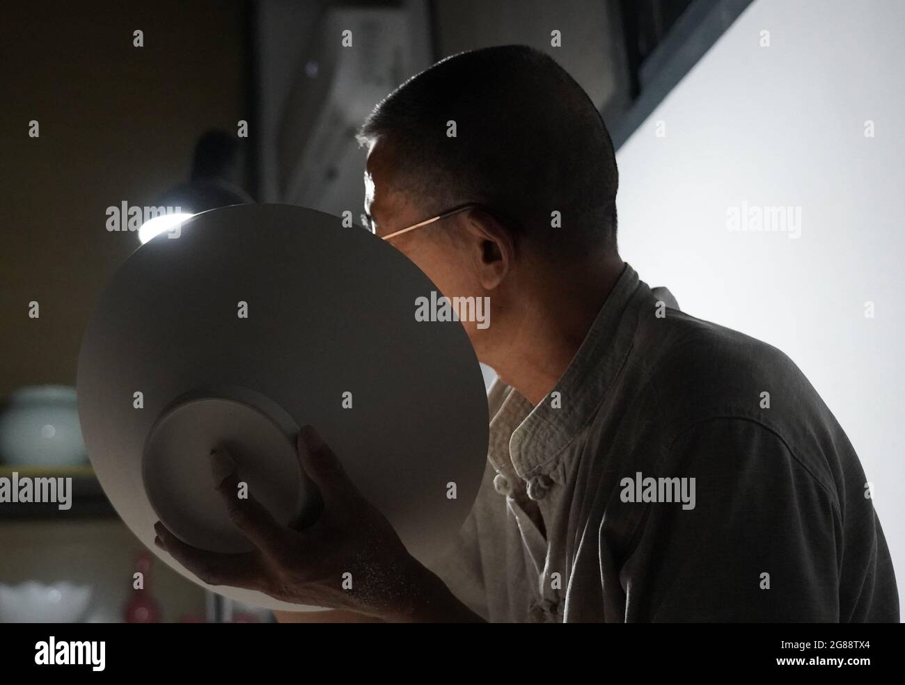 (210718) -- NANCHANG, 18 juillet 2021 (Xinhua) -- Xiong Guo'an vérifie l'épaisseur du corps d'une œuvre d'art en porcelaine coquillage en la frappant et en écoutant le son dans un studio de Jingdezhen, dans la province de Jiangxi, en Chine orientale, le 14 juillet 2021. La « porcelaine coquetier », célèbre pour son corps fin et transparent, présente le travail de main de haut niveau des maîtres à Jingdezhen. Xiong Guo'an, héritier de l'artisanat traditionnel en porcelaine coquetier, a commencé à apprendre l'art de son père quand il avait 12 ans. Ayant été dans l'industrie pendant 49 ans, il peut maintenant faire des œuvres d'art en porcelaine coquillage avec Banque D'Images
