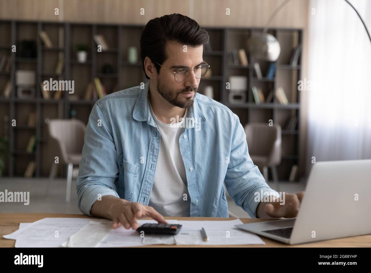 Jeune homme concentré calculant les dépenses domestiques, payant les factures en ligne. Banque D'Images