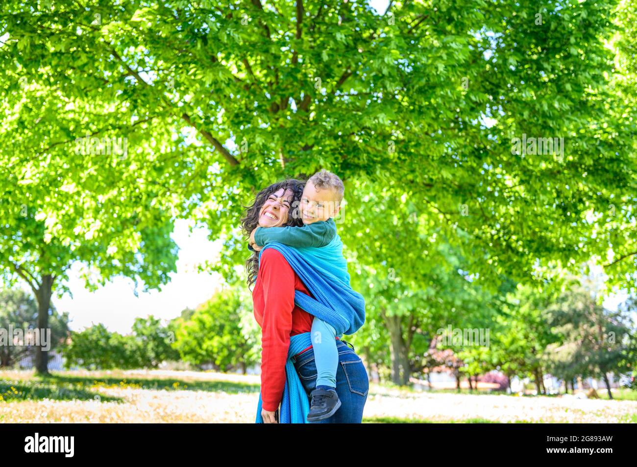 Une Jeune Mere Souriante Et Heureuse Porte Son Bebe Dans Une Elingue Est Debout Dans Un Parc Maman Et Son Fils Dans Une Elingue D Enveloppement De Bebe Qui Fait Froid Dehors