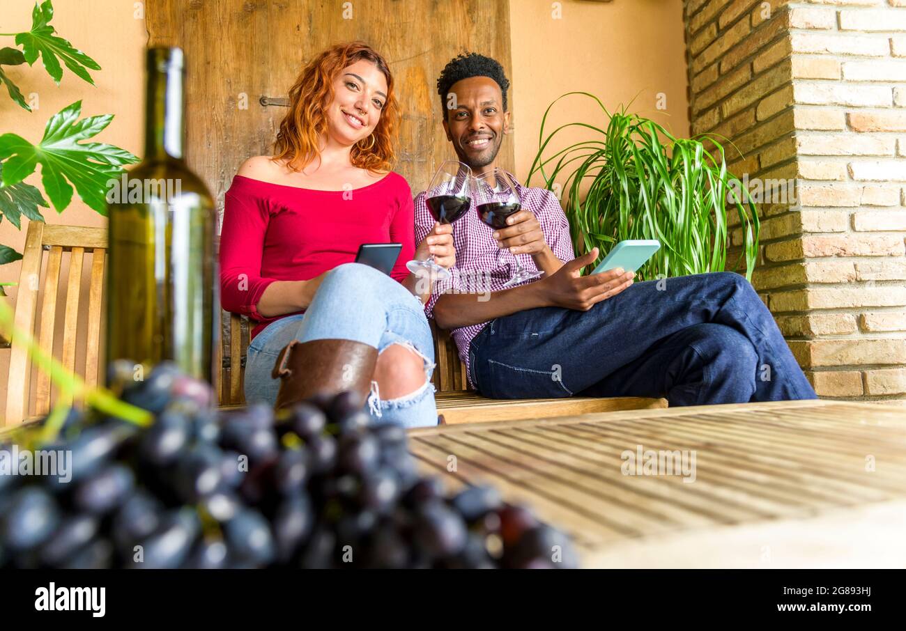 Un beau garçon et une belle fille adore boire du vin rouge et utiliser un smartphone dans le patio de la cave - couple multiethnique appréciant la dégustation de vin au restaurant Terra Banque D'Images
