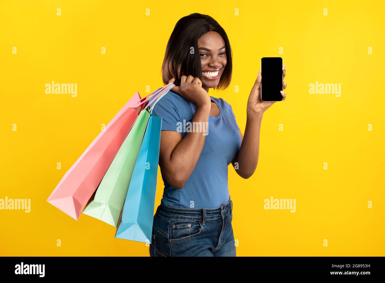 Noir lady montrant l'écran du téléphone contenant des sacs d'achats, fond jaune Banque D'Images