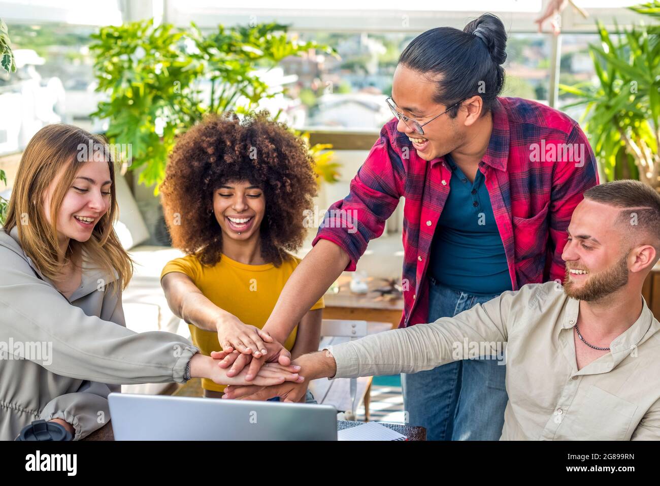 groupe diversifié d'amis célébrant avec un petit cinq la fin d'un projet de démarrage à l'intérieur assis sur un bureau. étudiants multiethniques les gens ensemble Banque D'Images