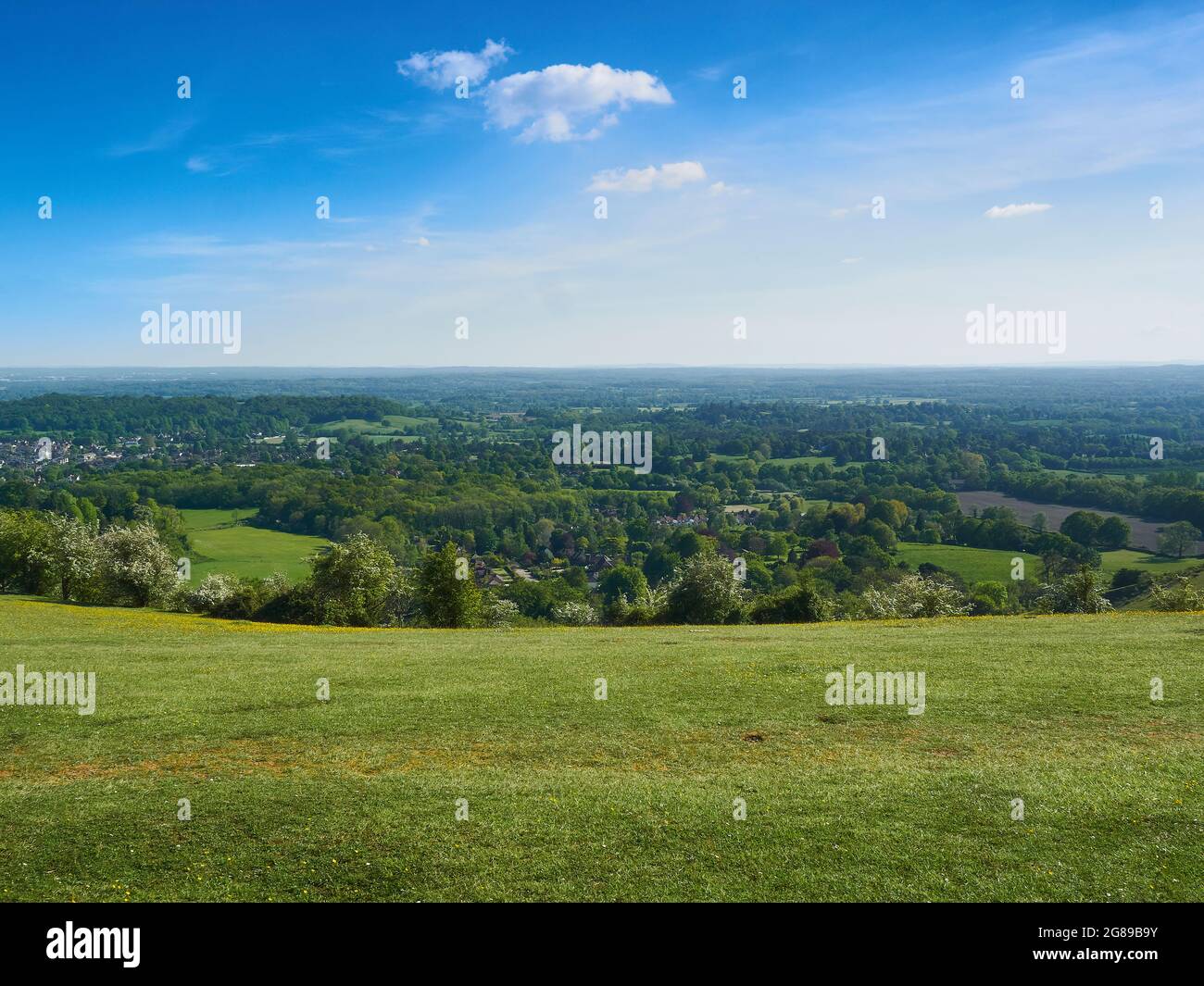 Un large ciel bleu nuageux, une colline verte herbeuse et les villes, les champs et les bois au large d'une vallée du Surrey. Banque D'Images