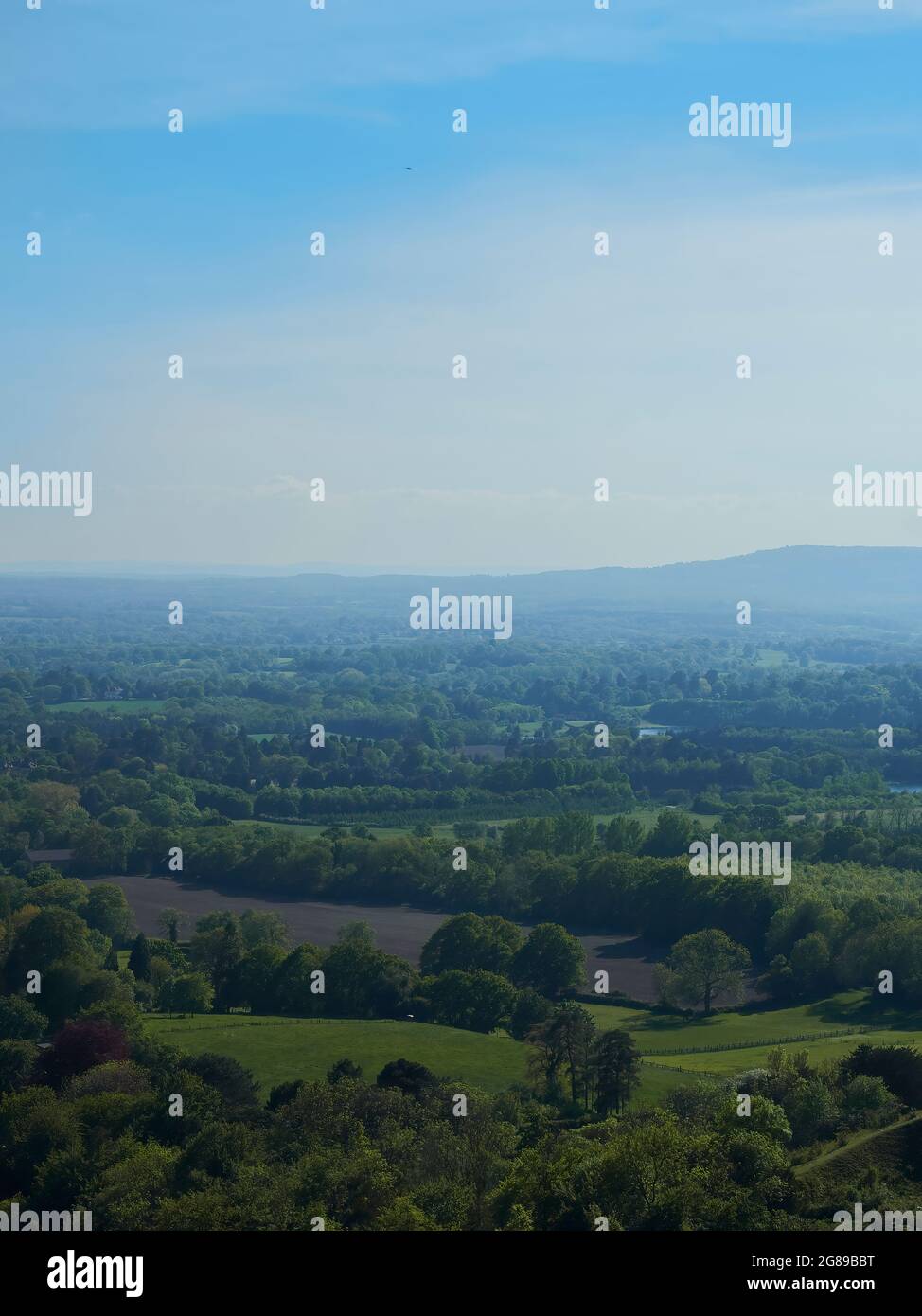 Vue claire et aérée sur une vallée bucolique, couverte de champs et de bois jusqu'à un horizon lointain, entouré de brume et bordé de collines. Banque D'Images
