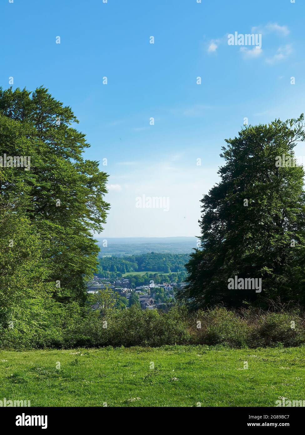 Vue sur le sommet d'une colline entourée d'arbres, sur une vallée verdoyante et bucolique de la campagne et des bois, sous un ciel bleu vif et estival. Banque D'Images