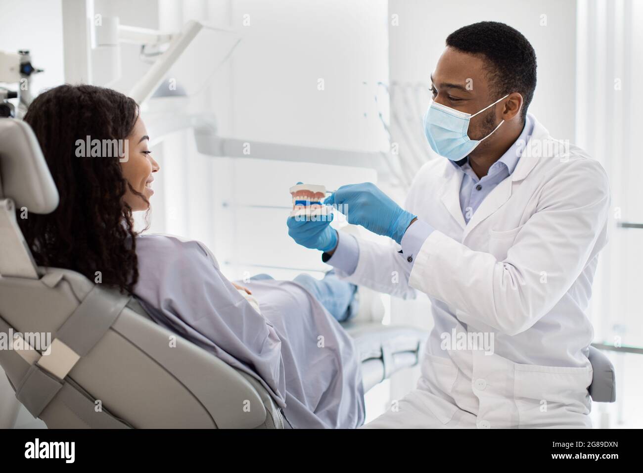 Stomatologue noir tenant une mâchoire en plastique et enseignant l'hygiène dentaire au patient féminin Banque D'Images