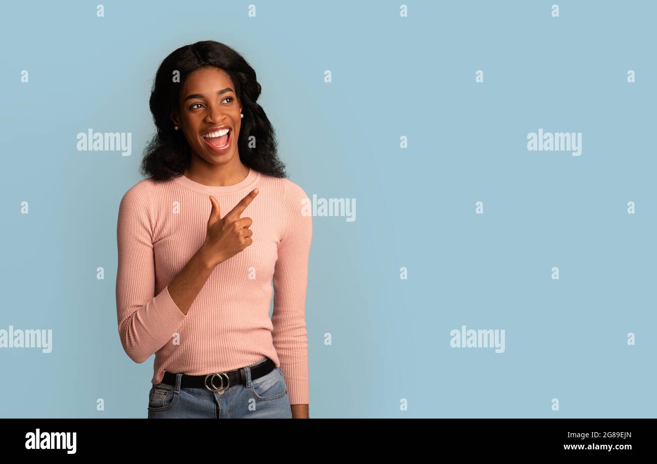 Offre exceptionnelle. Joyeuse jeune femme afro-américaine pointant du doigt et regardant de côté Banque D'Images
