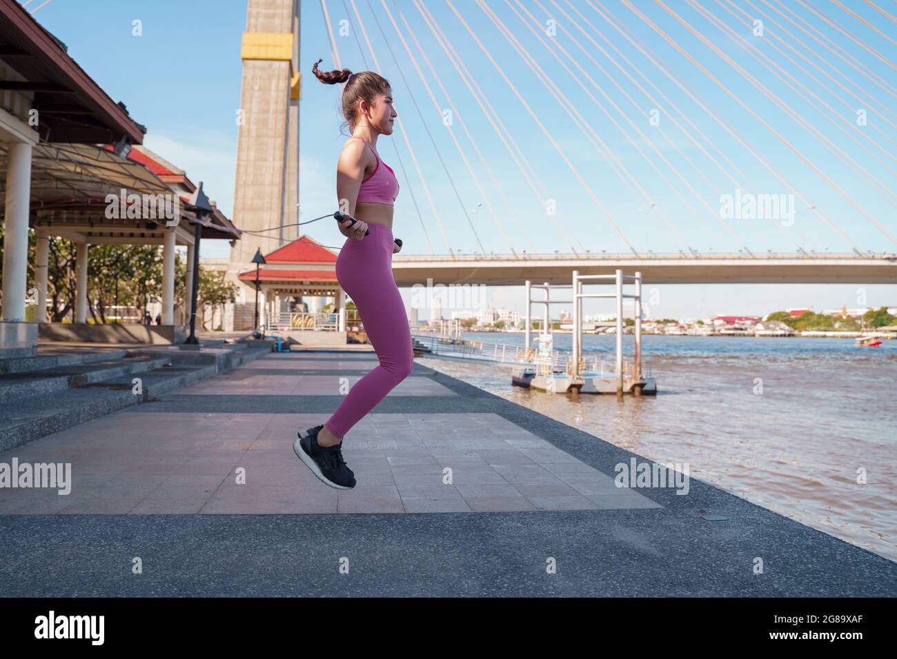FIT asiatique femme pratiquant l'entraînement cardio avec une corde à sauter pour la perte de poids. Jeune femme debout et face à la rivière au bord de la rivière sous le pont de la ville Banque D'Images