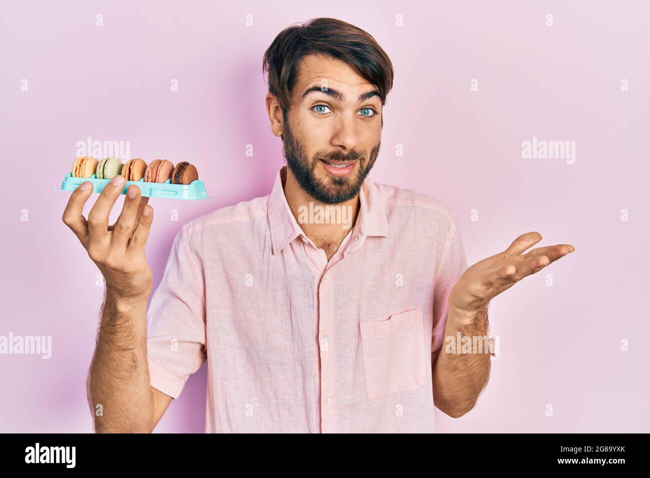 Jeune homme hispanique portant de délicieuses pâtisseries à base de macrons célébrant la réussite avec un sourire heureux et une expression gagnante avec une main levée Banque D'Images