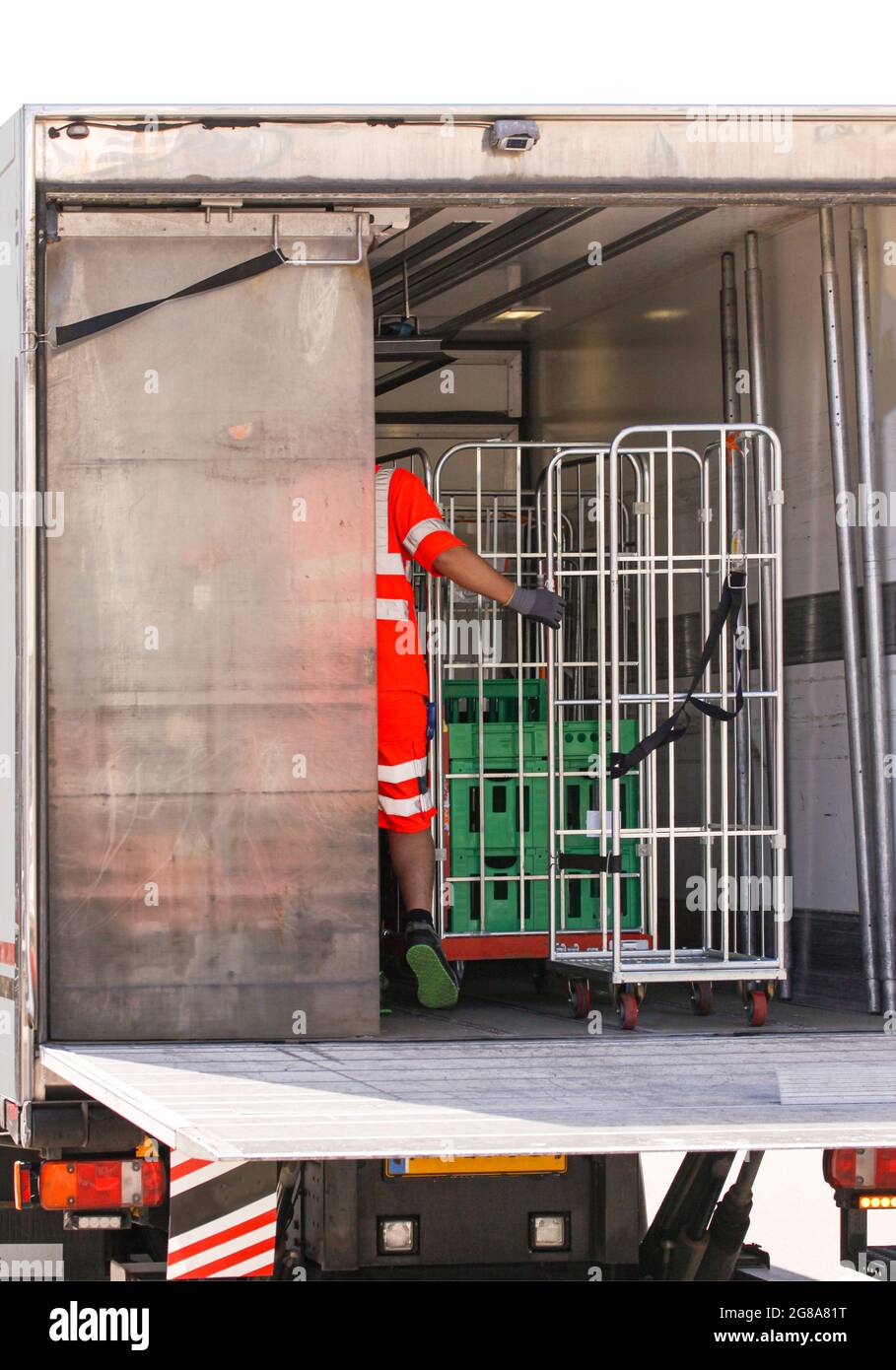 Homme d'origine africaine dans des vêtements de travail réfléchissants chargeant des produits laitiers dans des cages métalliques à partir d'une camionnette réfrigérée. Banque D'Images