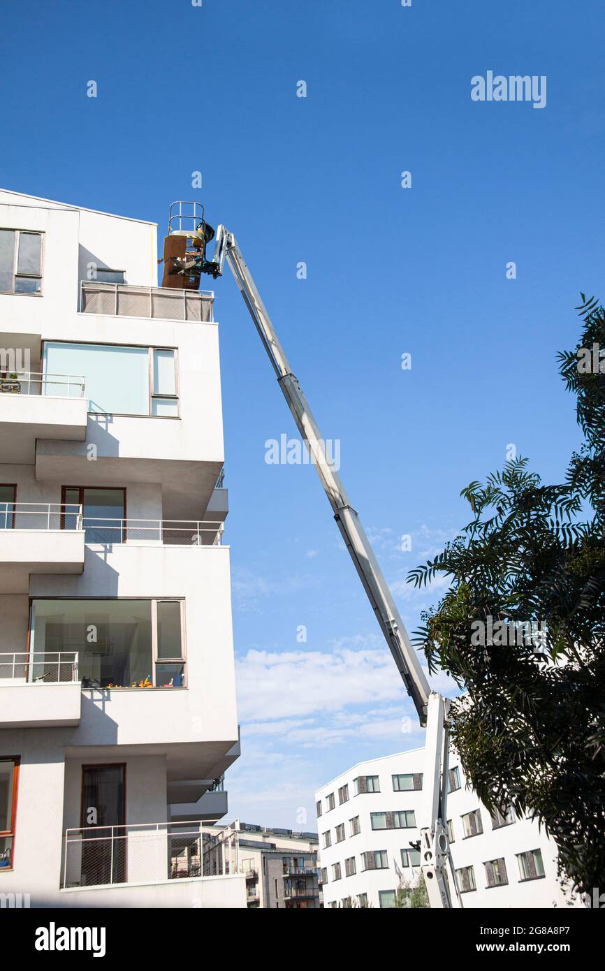Ouvriers d'entretien travaillant en hauteur à partir d'une rampe articulée, réparant la façade d'un bâtiment résidentiel. Fond bleu ciel. Barre omnibus industrielle Banque D'Images