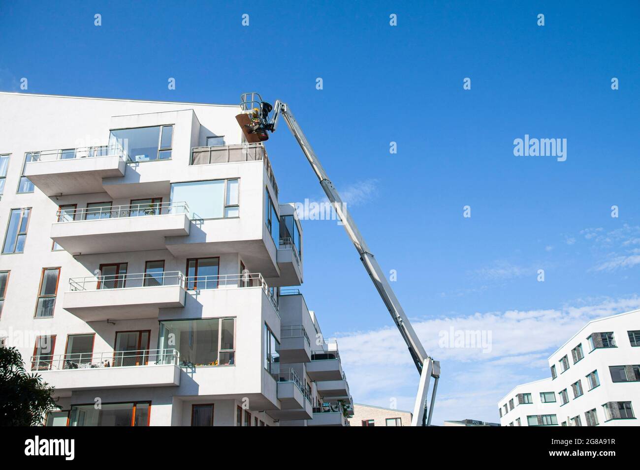 Ouvriers d'entretien travaillant en hauteur à partir d'une rampe articulée, réparant la façade d'un bâtiment résidentiel. Fond bleu ciel. Barre omnibus industrielle Banque D'Images