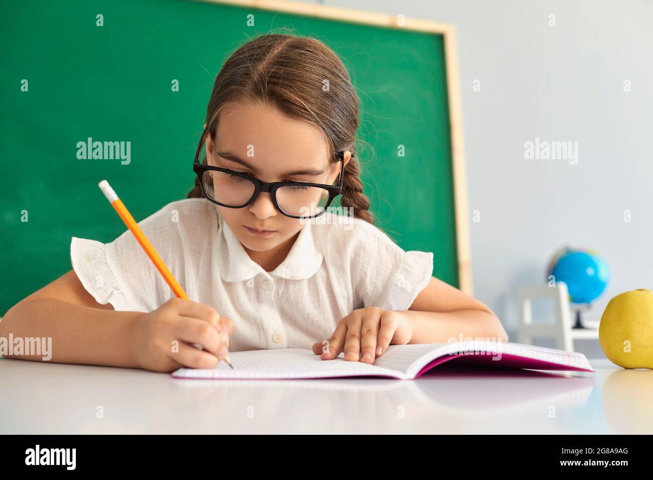 Élève à l'école. Une écolière intelligente dans ses yeux écrit dans un ordinateur portable dans une leçon de classe. Banque D'Images