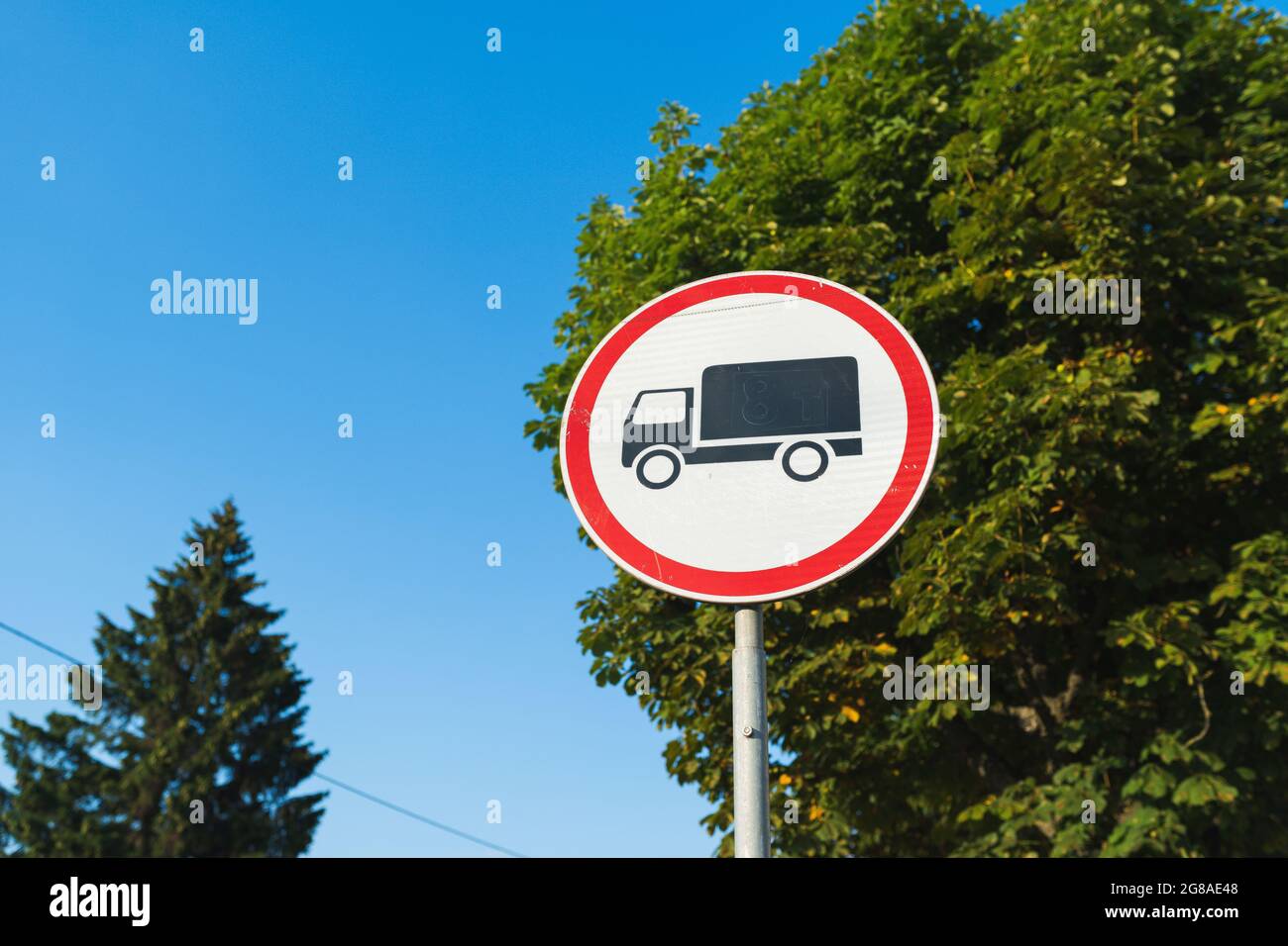 Panneau de signalisation rond rouge et blanc avec camion noir indiquant pas d'entrée pour les camions avec arbres et ciel bleu sur le fond Banque D'Images