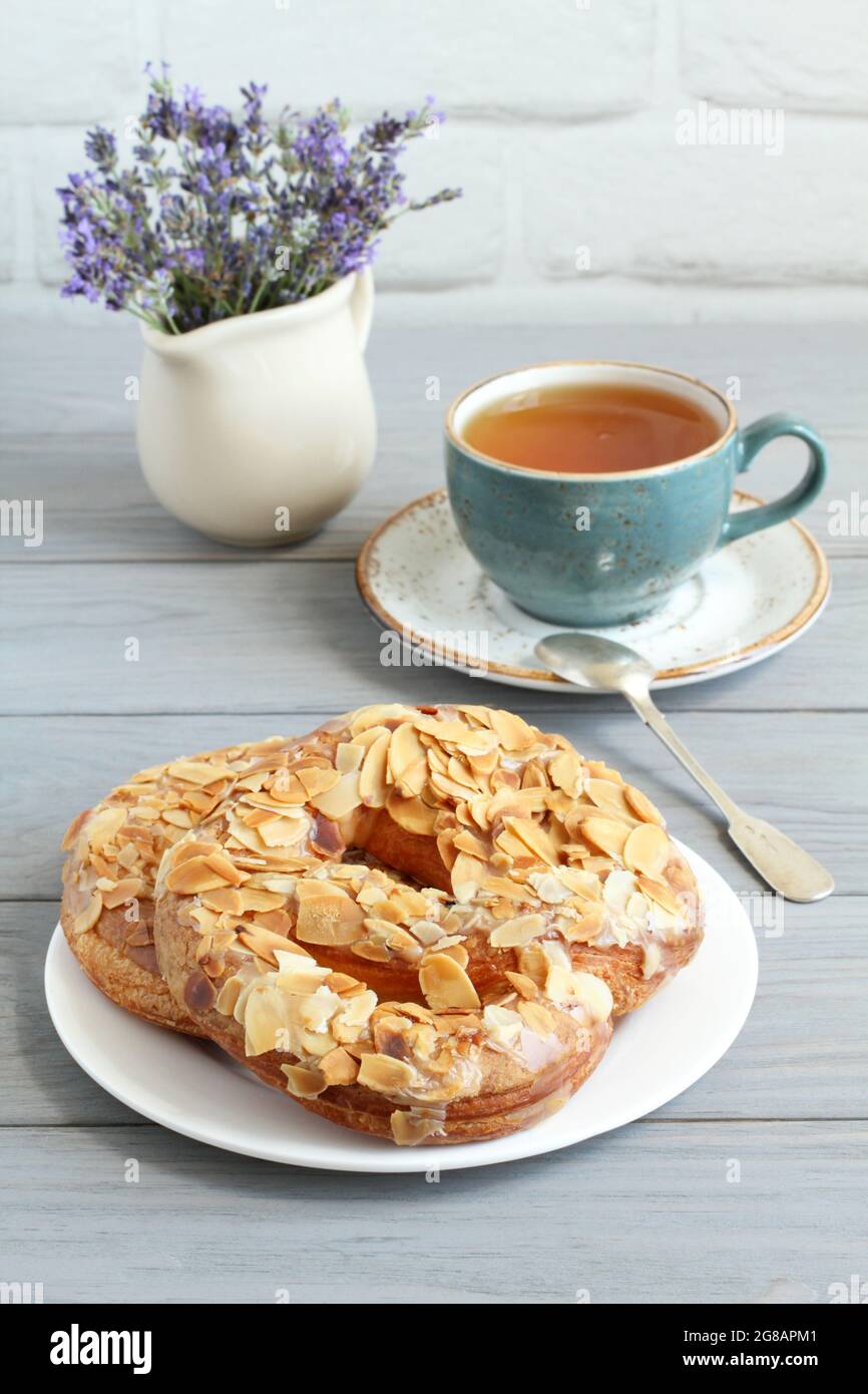 Bretzels parsemés d'amandes hachées et d'une tasse de tisane sur une table en bois gris. Gros plan Banque D'Images