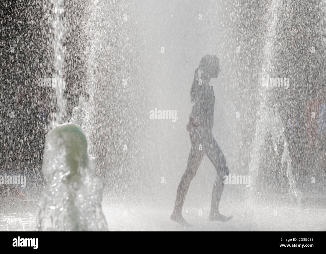 Silhouette d'une fille qui marche à travers une fontaine d'eau, en été Banque D'Images