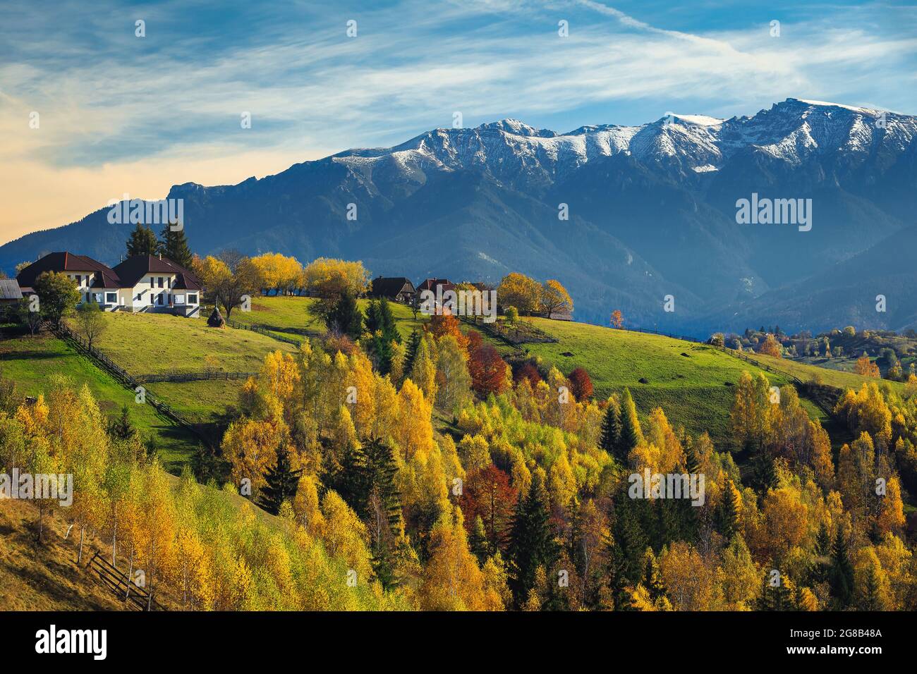 Paysage rural d'automne incroyable et bouleaux colorés sur les pistes. Maisons avec des jardins sur la colline et des montagnes enneigées en arrière-plan, Carpates, Banque D'Images