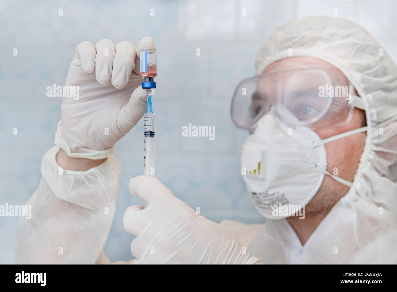 Gros plan d'un scientifique qui interagit avec une seringue et un flacon en verre de vaccin liquide en laboratoire. Banque D'Images