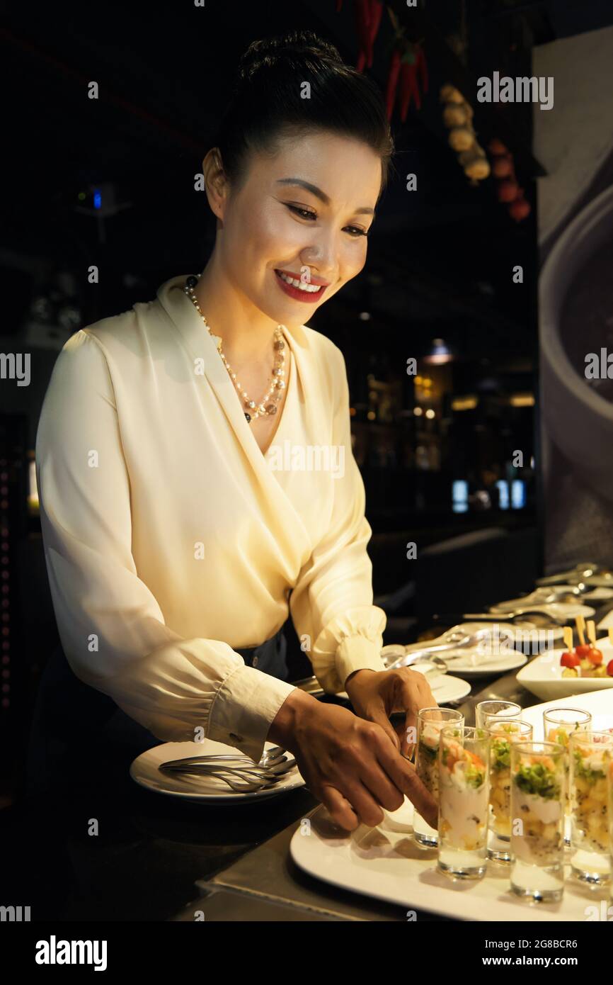Un beau directeur de restaurant souriant qui vérifie de délicieux hors-d'œuvre est prêt à servir Banque D'Images