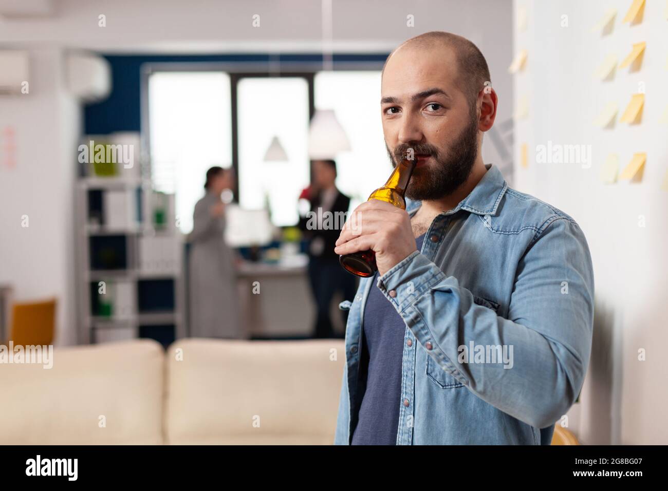 Homme buvant une bouteille de bière après une réunion de travail avec des collègues pour le plaisir. Célébration gaie avec des collègues au bureau tout en mangeant et en buvant de l'alcool. Des amis heureux qui font la fête Banque D'Images