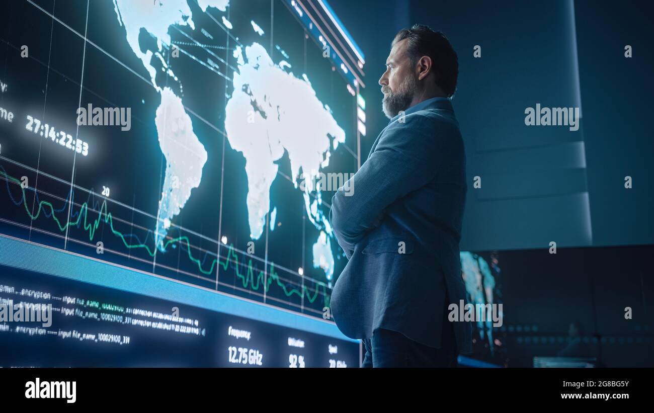 Ingénieur informatique senior regardant l'écran géant montrant une carte globale avec des points de données. Système de la société de technologie des télécommunications Banque D'Images