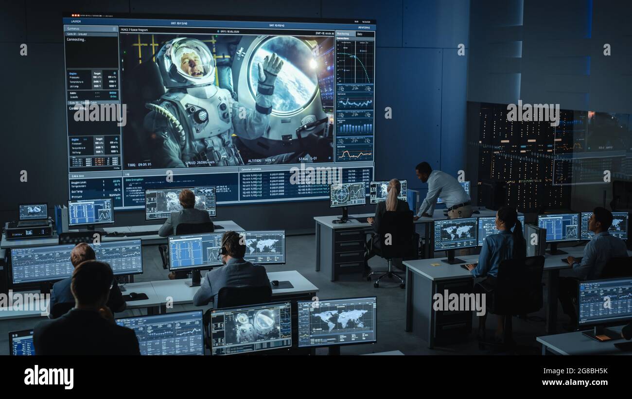 Groupe de personnes dans le centre de contrôle de mission établir une connexion vidéo réussie sur un grand écran avec un astronaute à bord d'une station spatiale. Vol Banque D'Images