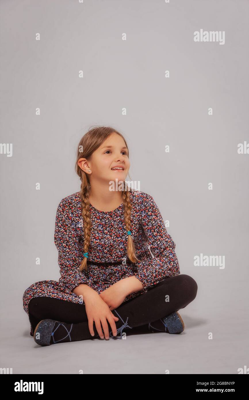 Petite fille riante assise à pattes croisées sur le sol, isolée sur blanc. Banque D'Images