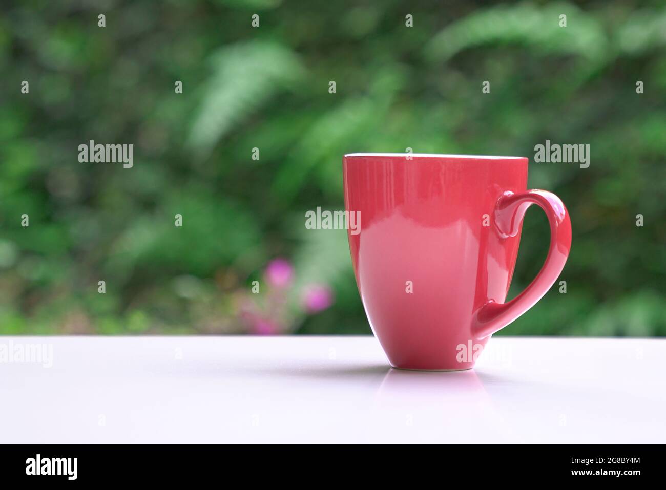 Café chaud dans une tasse rouge sur une table avec fond de bokeh nature. Copier l'espace. Banque D'Images