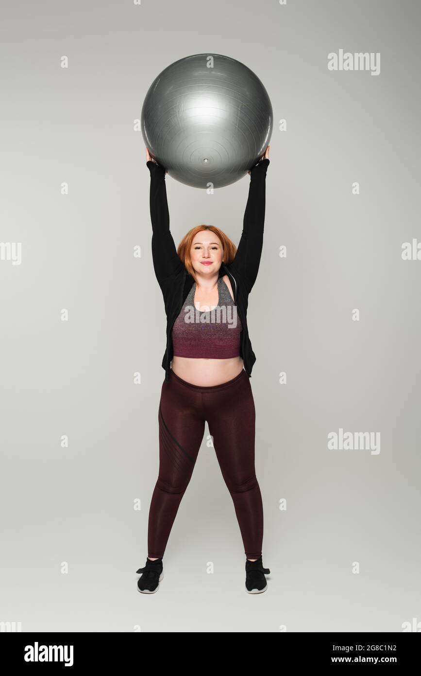Femme de taille plus tenant le ballon de fitness sur fond gris Banque D'Images