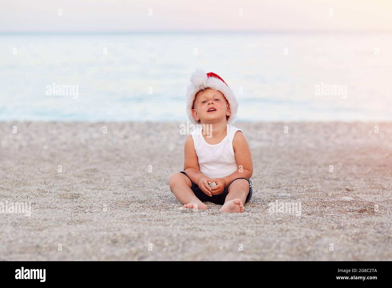 Un petit garçon caucasien célèbre la Saint-Sylvestre ou Noël sur la plage, en bord de mer. Concept de vacances, ambiance de Noël. Photo de haute qualité Banque D'Images