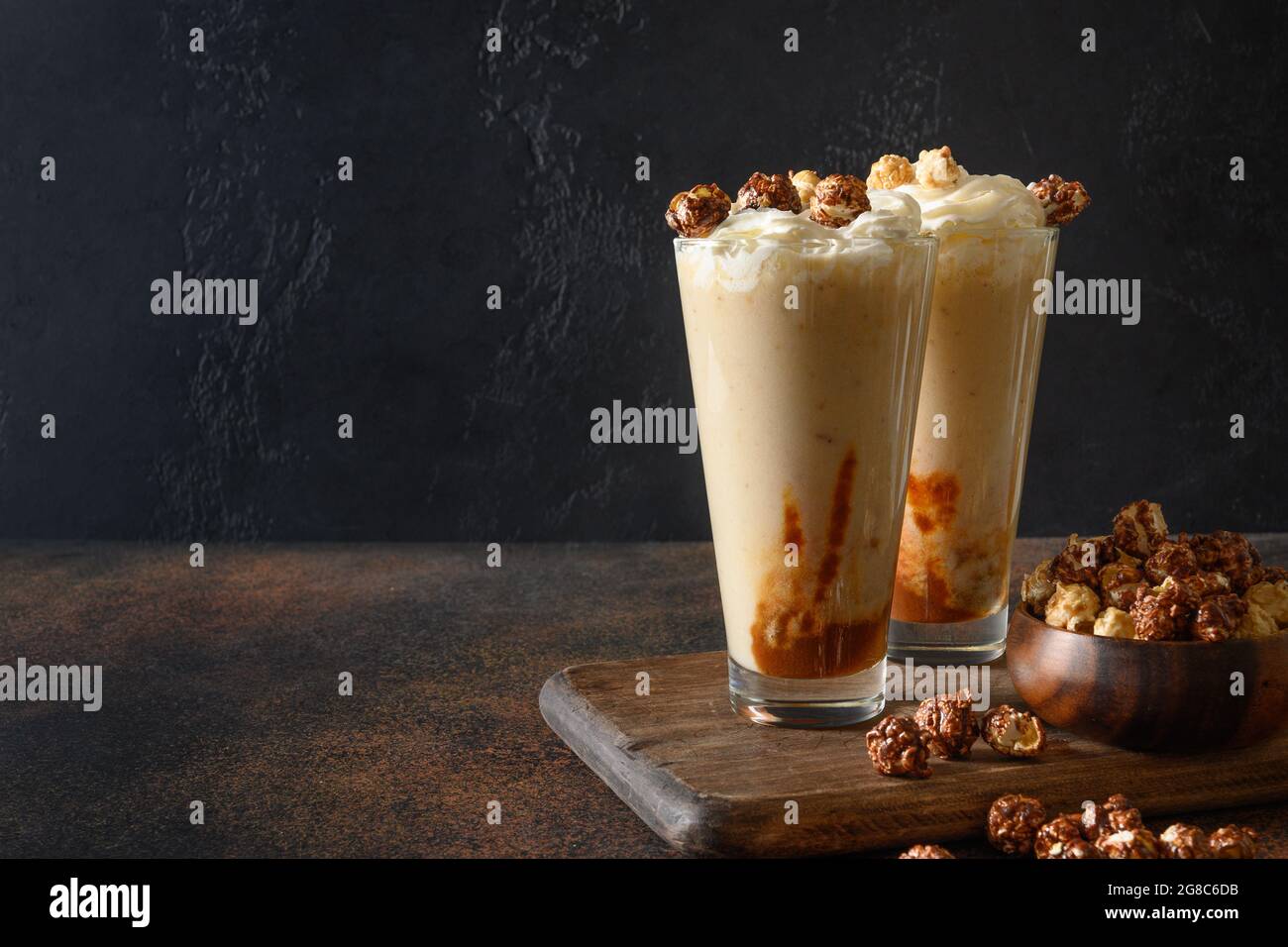 Délicieux milkshake à la banane garni de caramel, crème fouettée, pop-corn sur fond sombre. Format vertical Banque D'Images