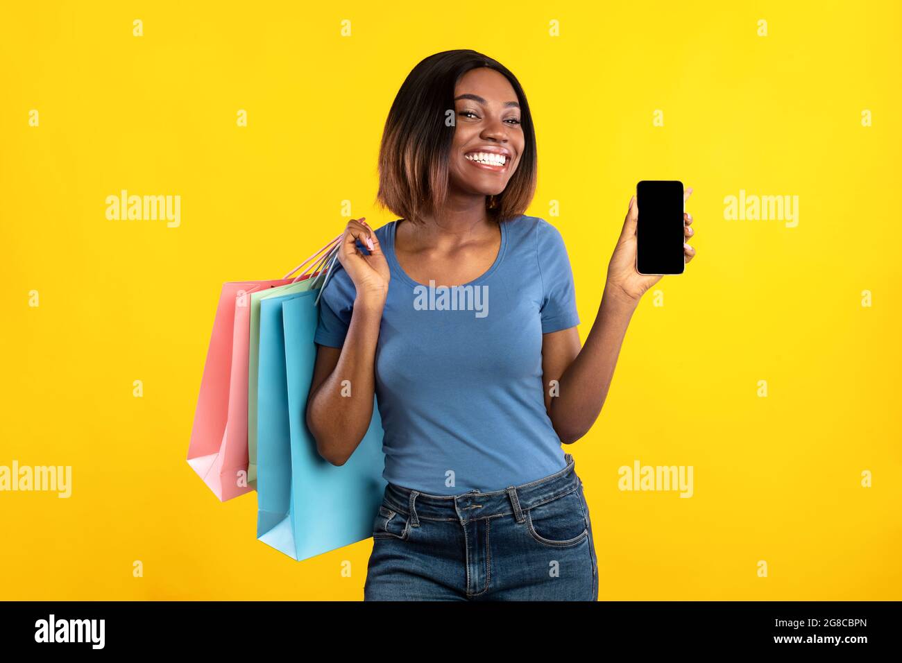 Femme africaine montrant l'écran de smartphone posant avec des sacs de Shopper, Studio Banque D'Images