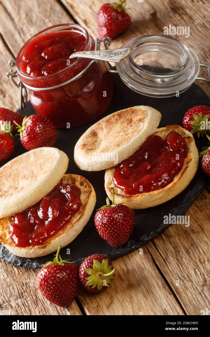 Muffins anglais avec confiture de fraises en gros plan sur la table, style rustique. Vertical Banque D'Images