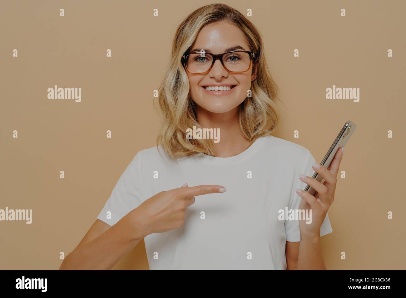 Portrait d'une jeune femme blonde impressionnée et excitée montrant quelque chose d'impressionnant sur son écran de téléphone Banque D'Images