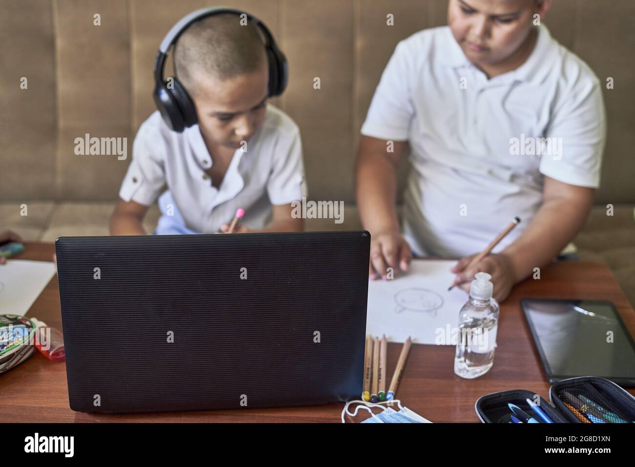 Les jeunes élèves de sexe masculin dessinant tout en écoutant le cours d'art en ligne sur un ordinateur portable à la maison Banque D'Images