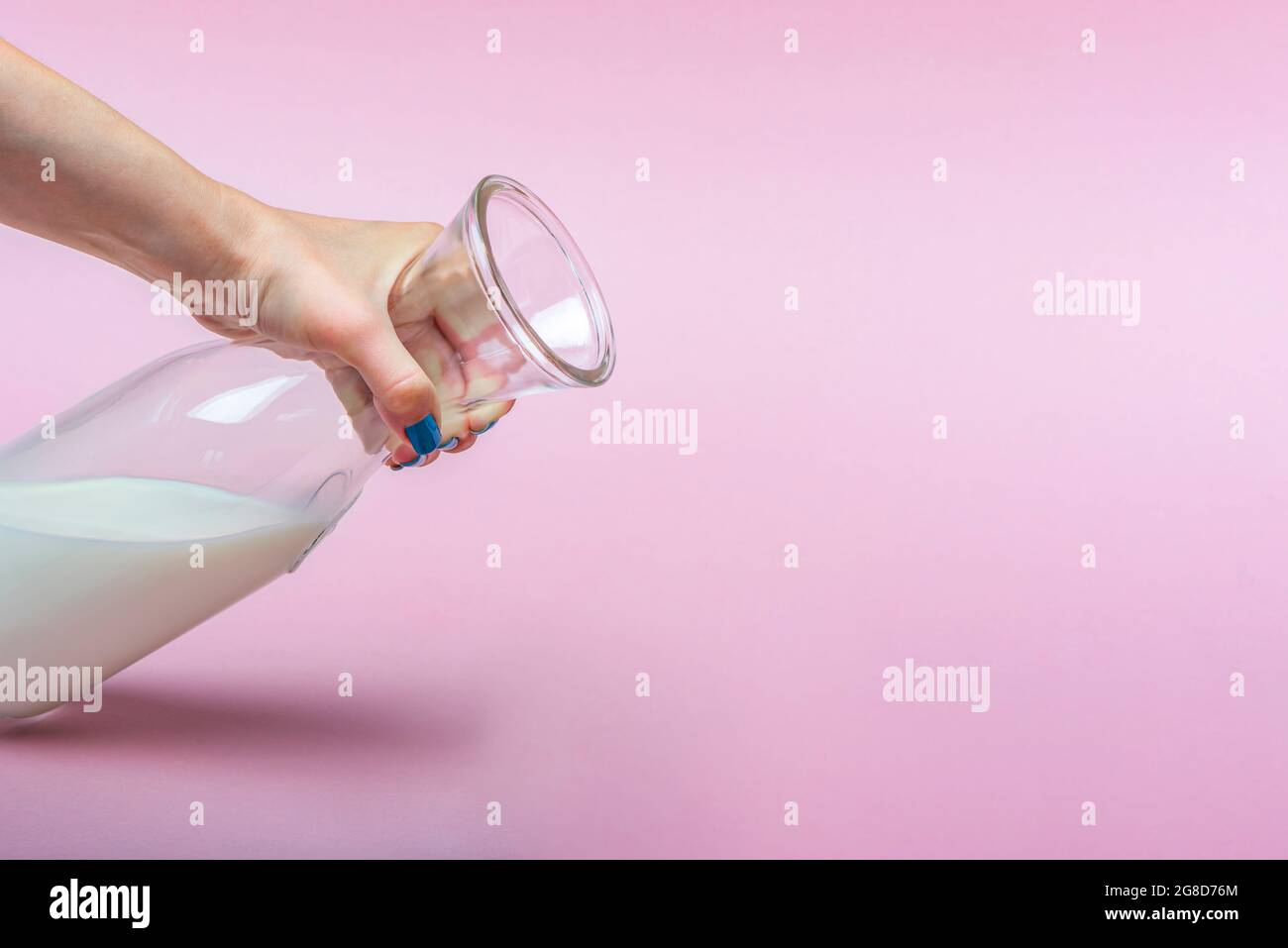 Un pot de lait sur fond rose dans la main d'une femme. Lait dans une bouteille en verre. Espace pour le texte, grande bannière. Banque D'Images