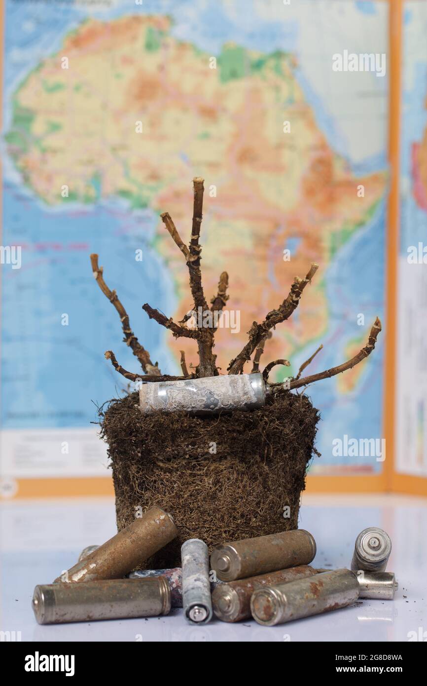 Une plante morte avec un caillot de terre. Batteries corrodées autour de. En arrière-plan, une carte de l'Afrique est hors de point central. Recyclage des déchets et environnement pro Banque D'Images