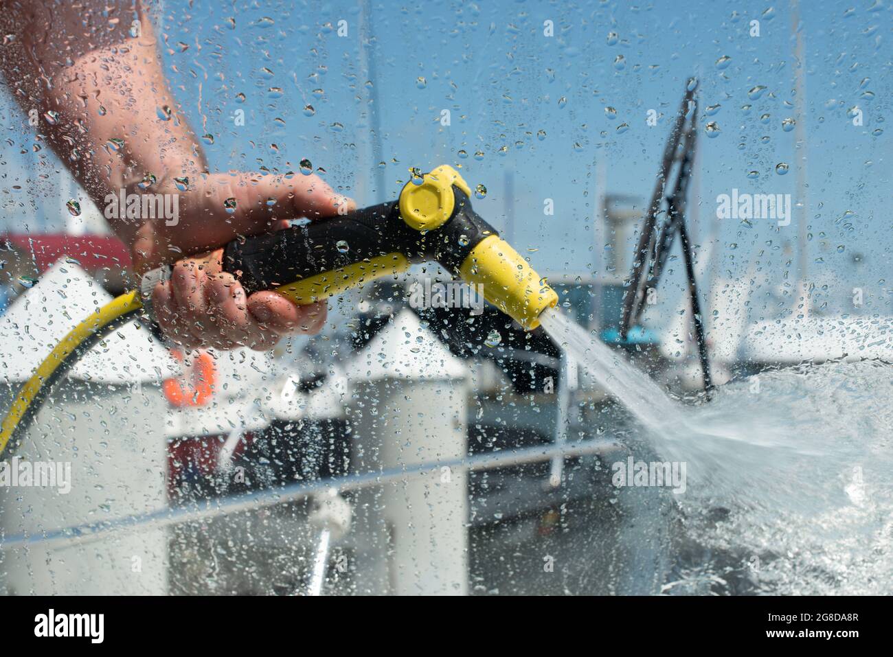 Main tenant le pistolet de pulvérisation d'eau. Homme lavant bateau avec système d'eau sous pression. Vue depuis l'intérieur du bateau. Concentrez-vous sur les gouttes d'eau. Concept de maintenance de yacht. Banque D'Images