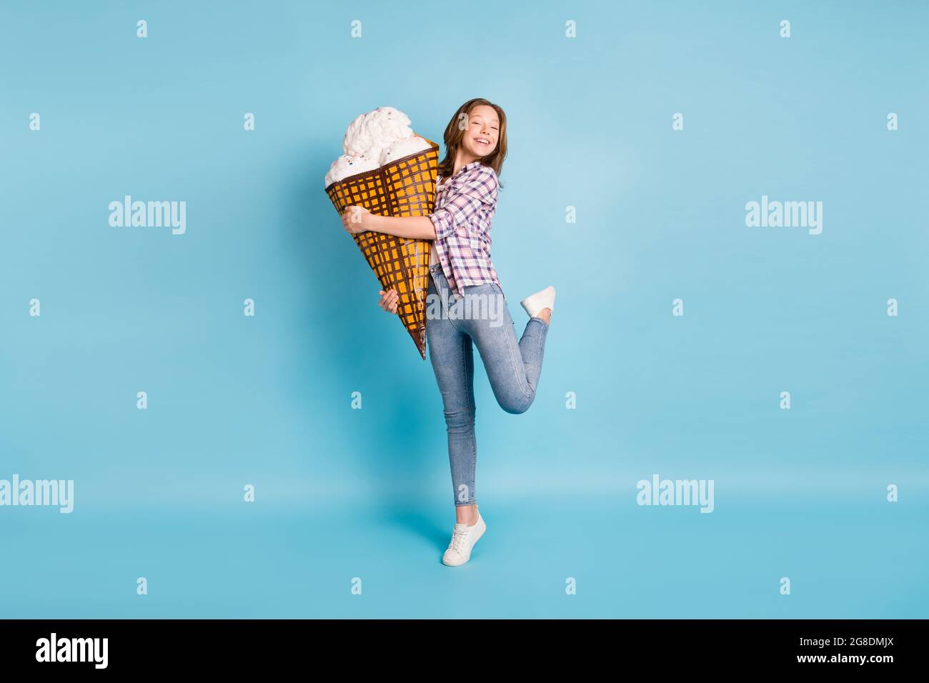 Photo pleine grandeur de la petite fille positive debout sur la pointe orteil tenir grande glace isolée sur fond bleu Banque D'Images